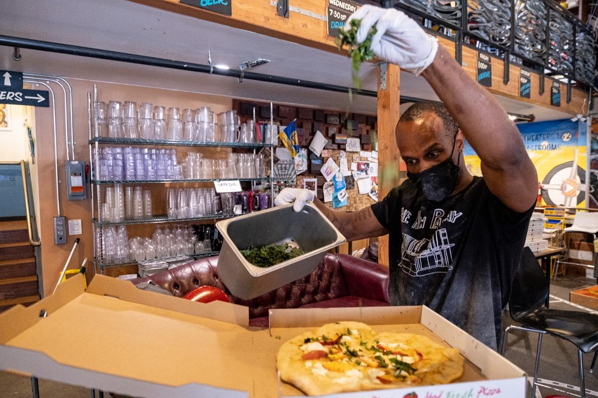 New Parkway employee Italo B sprinkles chopped basil onto a pizza made for the New Parkway's food program. August 12, 2020. Photo: Pete Rosos